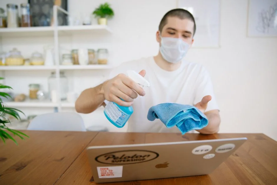 Anonymous male wearing yellow latex gloves and dark t shirt wiping mirror in bathroom with paper napkin